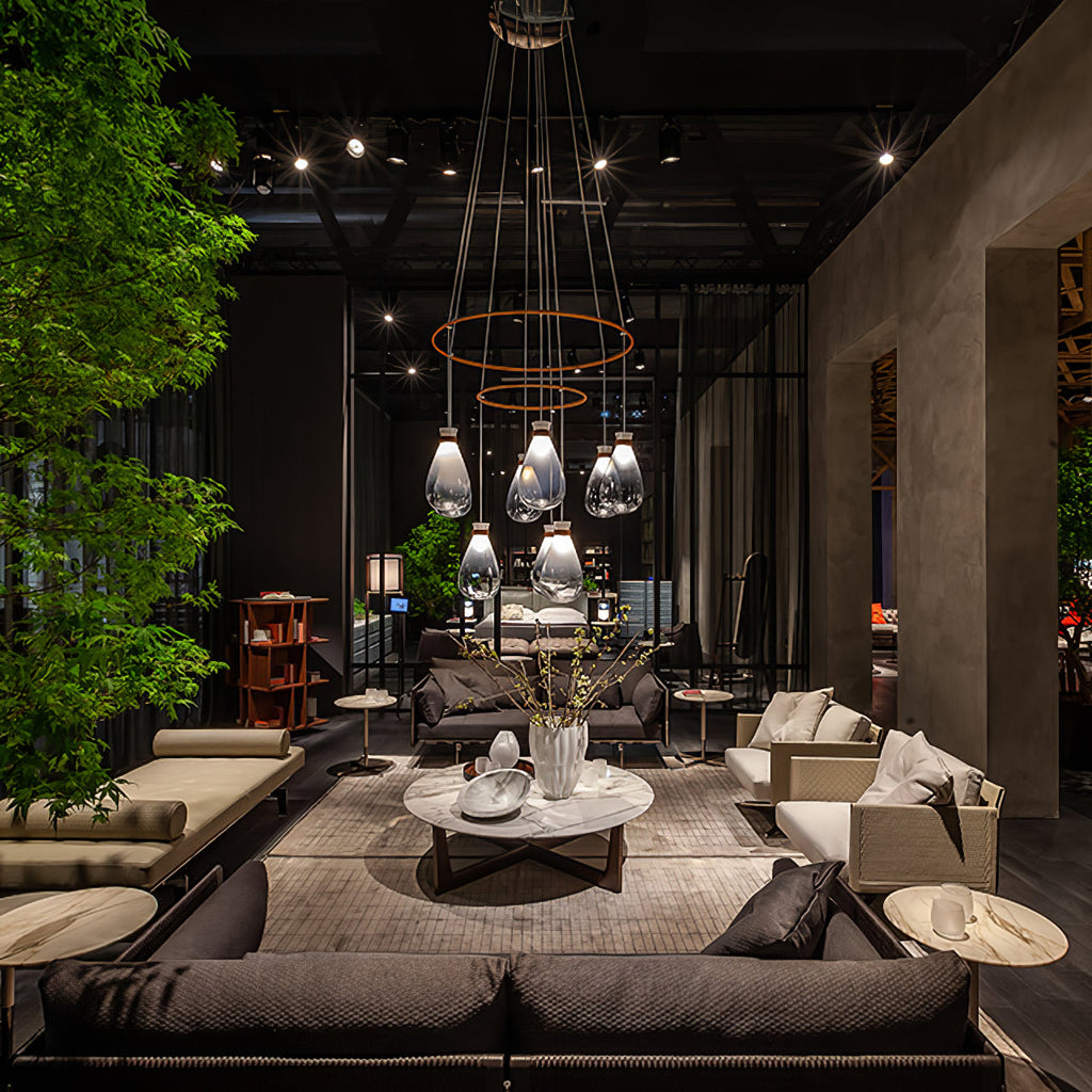 Clérachic teardrop pendants hung in tiers from copper rings above a lounge with a low marble table, in a dark showroom.