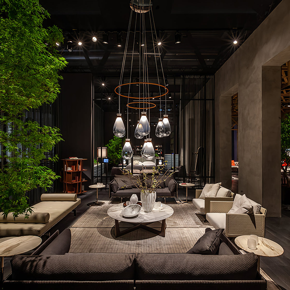 Clérachic teardrop pendants hung in tiers from copper rings above a lounge with a low marble table, in a dark showroom.