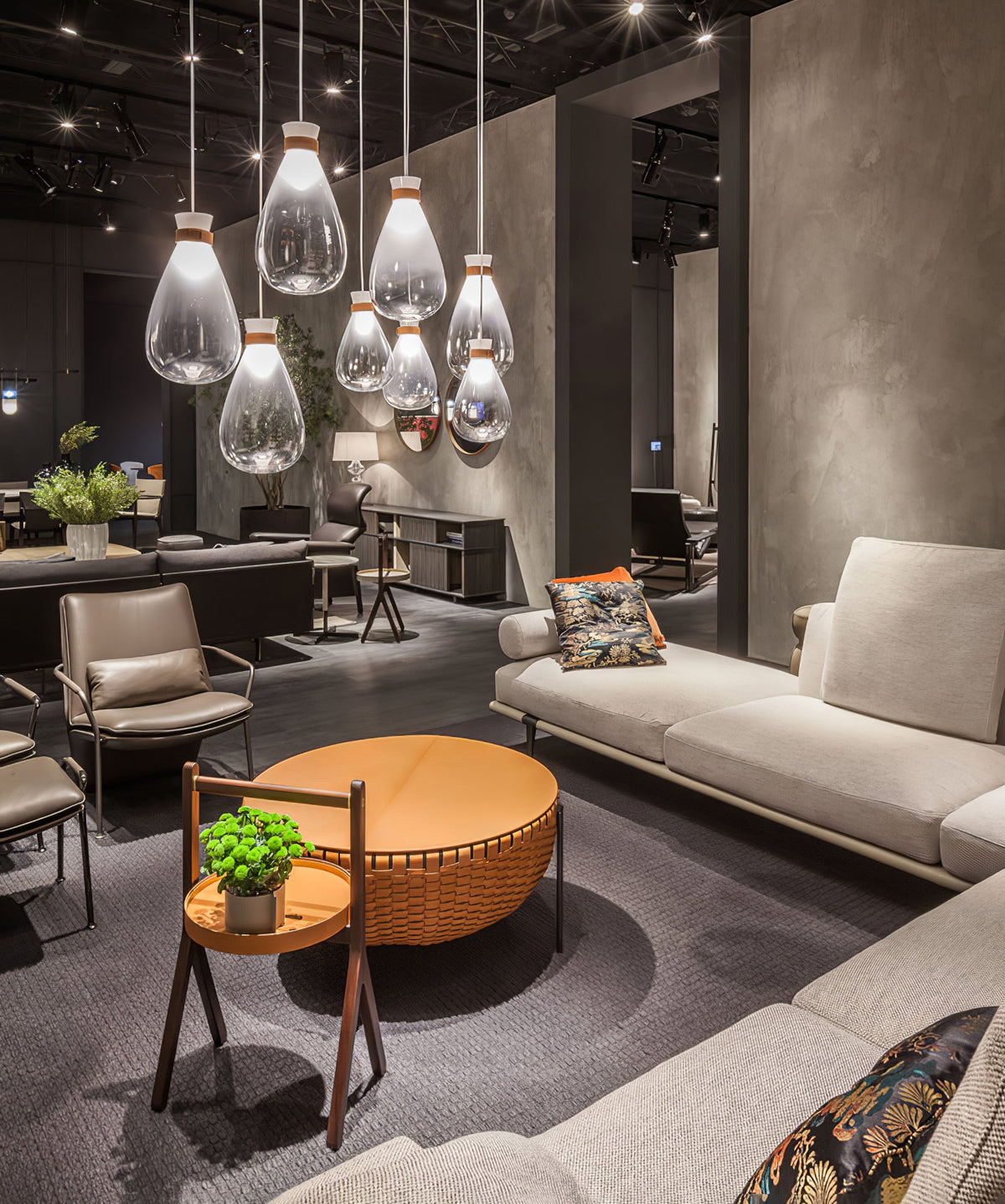 Clear glass Clérachic teardrop pendants with leather-strapped necks hanging above a round tan table and a grey sofa.