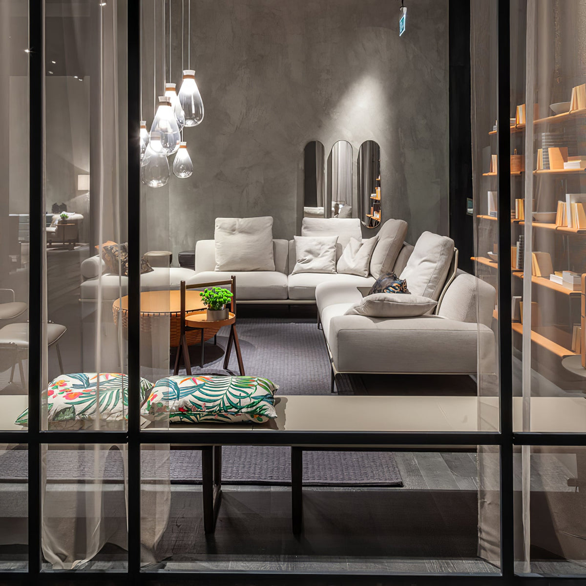 Clérachic teardrop pendants glimpsed through a glass partition, above a grey sofa and shelves with orange-edged boards.