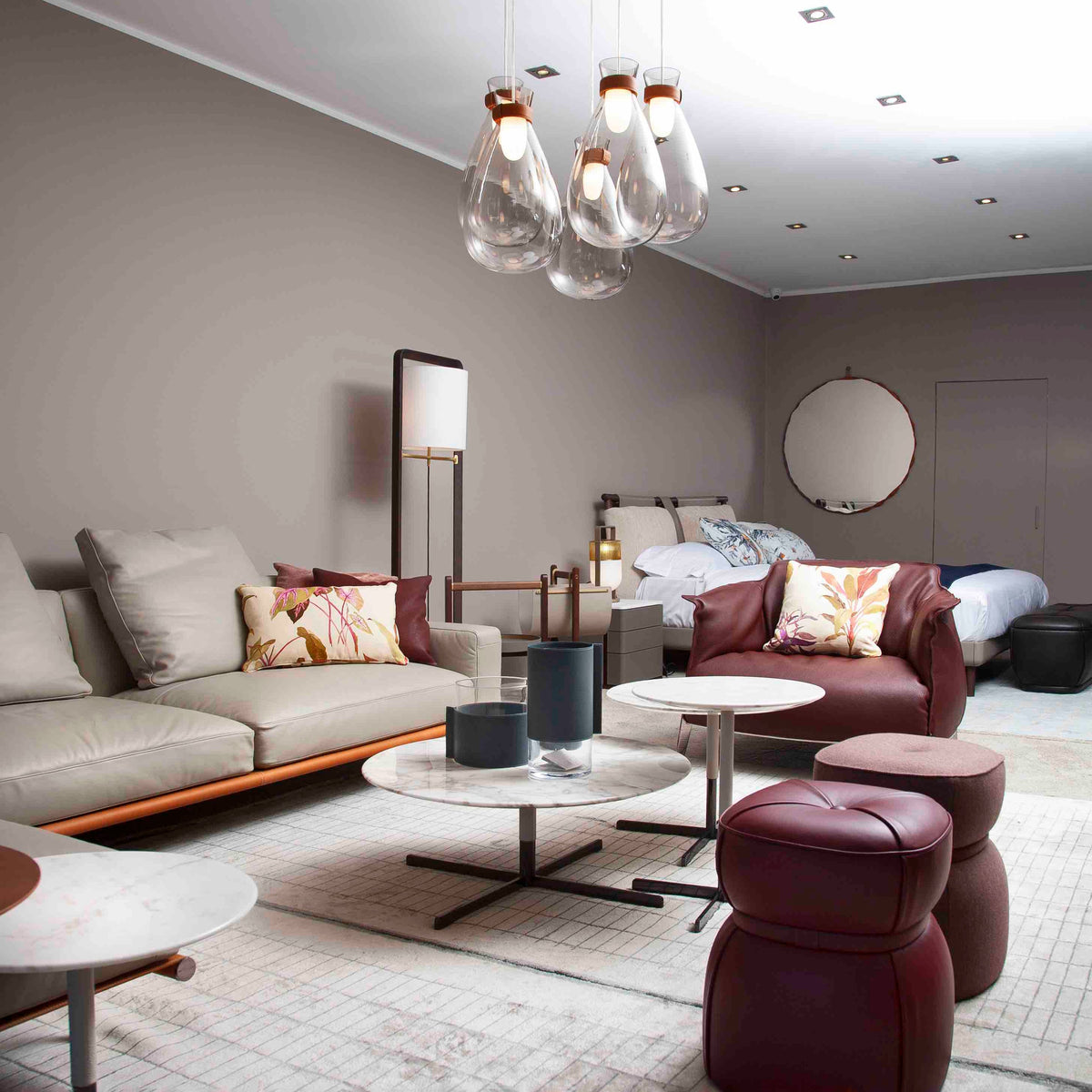 Cluster of clear glass Clérachic teardrop pendants over a living area with a leather sofa, round tables and burgundy poufs.
