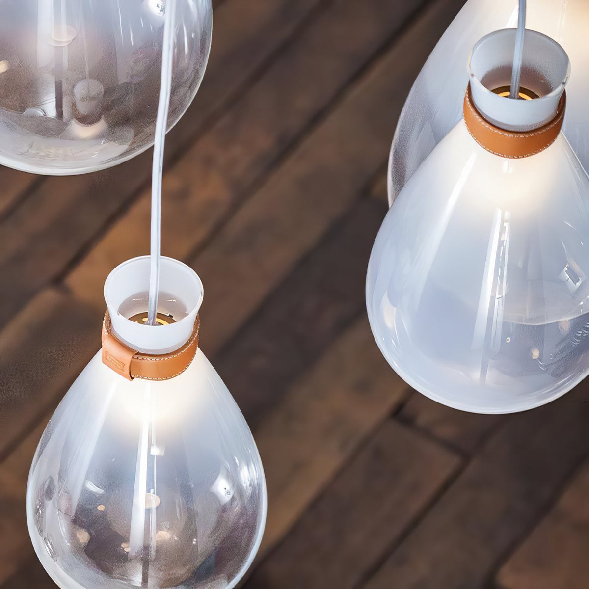 Looking down on Clérachic teardrop pendants with leather-strapped necks, over a dark wooden plank floor.