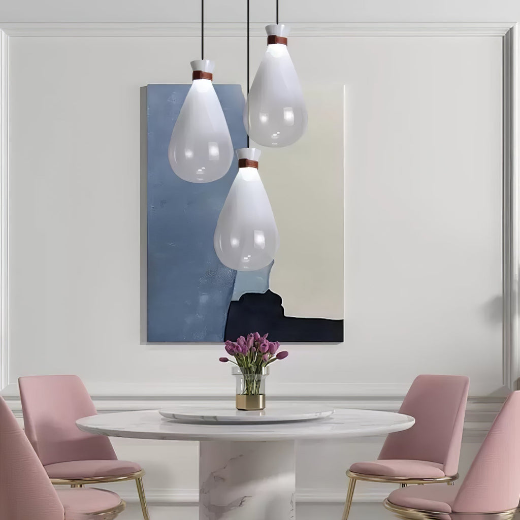 Three white Clérachic teardrop pendants over a round marble table with pink chairs, in front of a blue abstract painting.