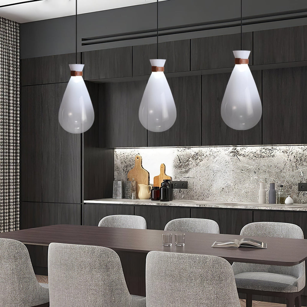 Three white Clérachic teardrop pendants above a dark dining table with grey chairs, in a kitchen with a stone splashback.