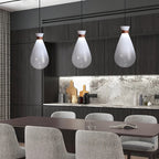 Three white Clérachic teardrop pendants above a dark dining table with grey chairs, in a kitchen with a stone splashback.
