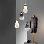 Four Clérachic teardrop pendants, some white and some grey-toned, hanging at varied heights beside a mannequin in a dark coat.