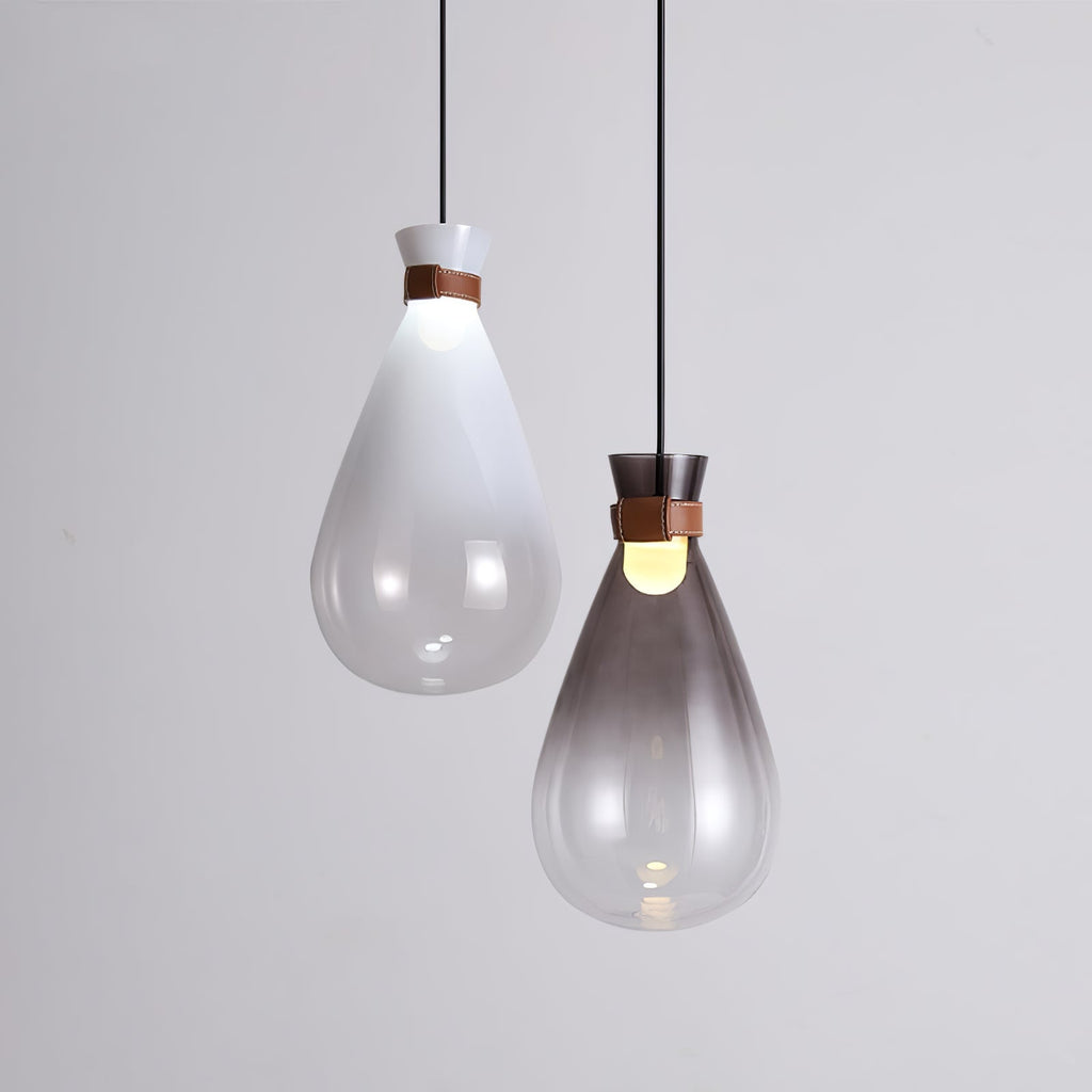 A white and a smoke-grey Clérachic teardrop pendant side by side against a pale grey wall, each with a leather strap.