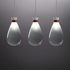 Three grey-gradient Clérachic teardrop pendants in a row, lit at the neck, against a dark grey backdrop.