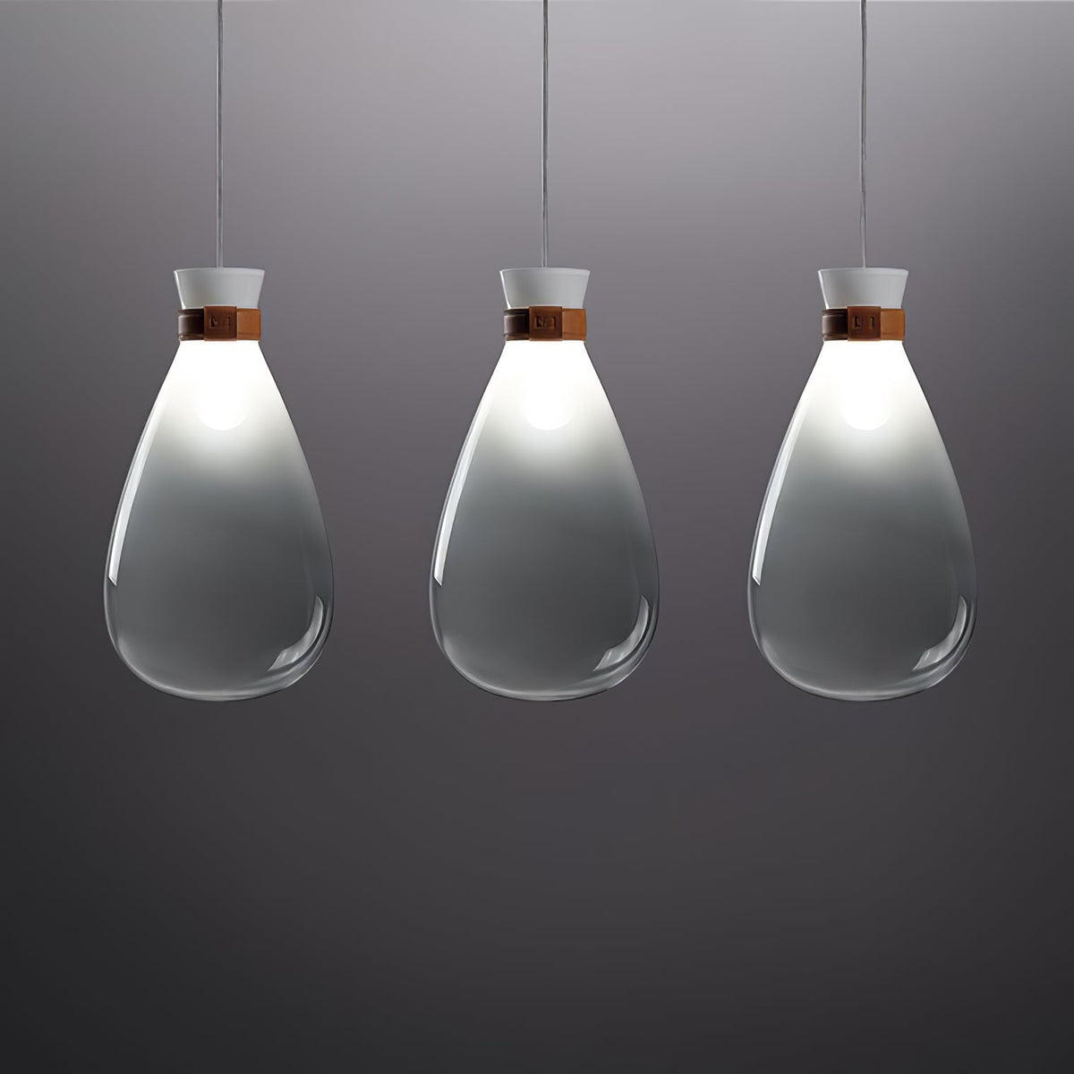 Three grey-gradient Clérachic teardrop pendants in a row, lit at the neck, against a dark grey backdrop.