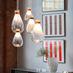 Cluster of Clérachic teardrop pendants with warm glowing necks, hung before striped red-and-white framed prints and a brick wall.