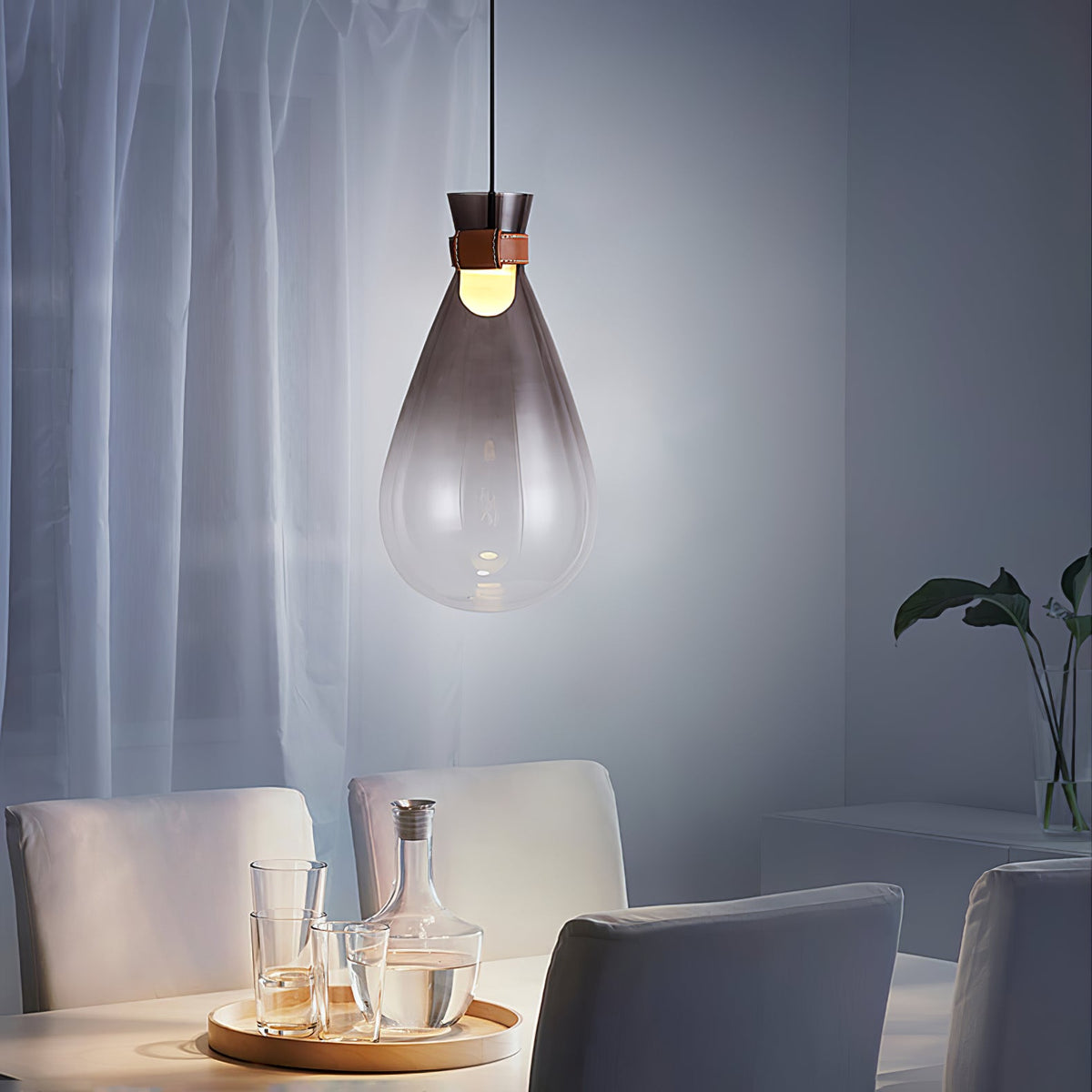 Smoke-grey Clérachic teardrop pendant in a cool, blue-lit room, above a table with glasses and a carafe on a wooden tray.