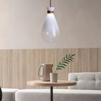 White Clérachic teardrop pendant above a small round wooden table, with a jug and a leafy stem against a slatted wall.