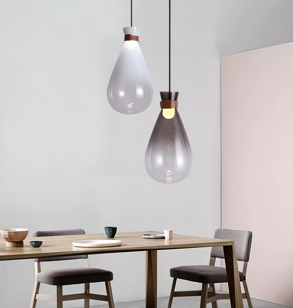 A clear and a smoke-grey Clérachic teardrop pendant hanging over a wooden dining table with grey chairs and a pink wall.