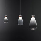 Three Clérachic teardrop pendants in three sizes, fading from white to smoke grey, hanging against a dark charcoal wall.