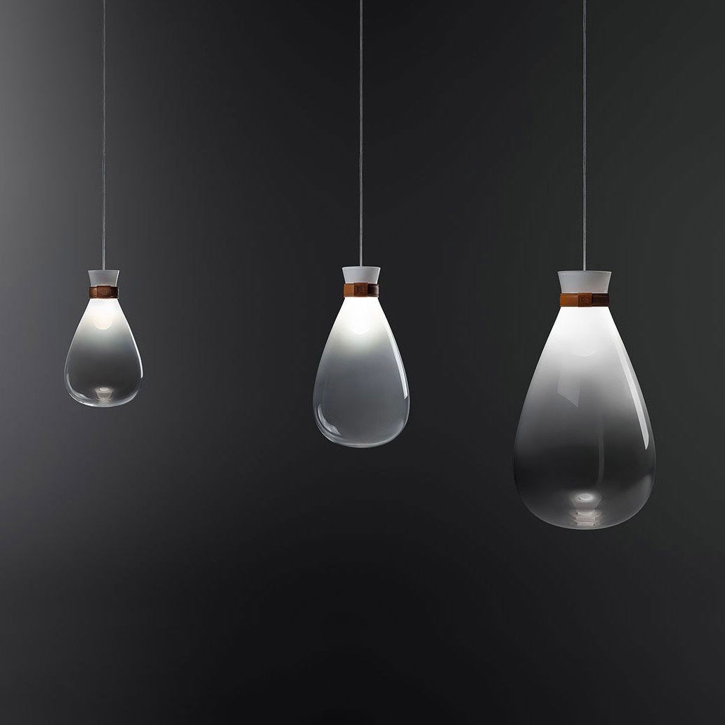 Three Clérachic teardrop pendants in three sizes, fading from white to smoke grey, hanging against a dark charcoal wall.