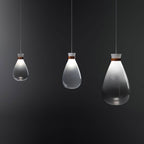 Three Clérachic teardrop pendants of different sizes, clear and grey-gradient glass with leather straps, against a dark backdrop.