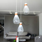 Three clear and frosted Clérachic teardrop pendants with leather straps, over a grey sofa in a showroom with track lights.