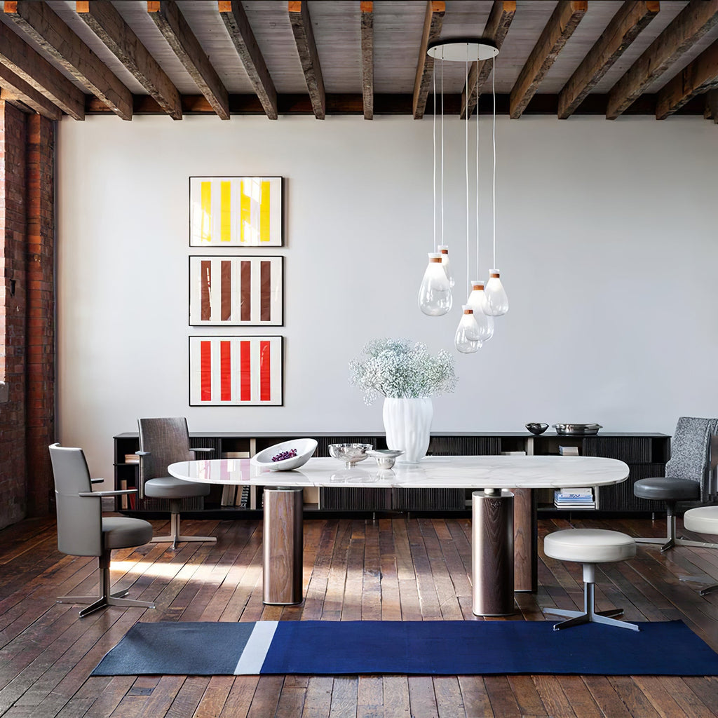 Cluster of Clérachic teardrop pendants over a long oval table in a loft with exposed beams, with striped prints behind.