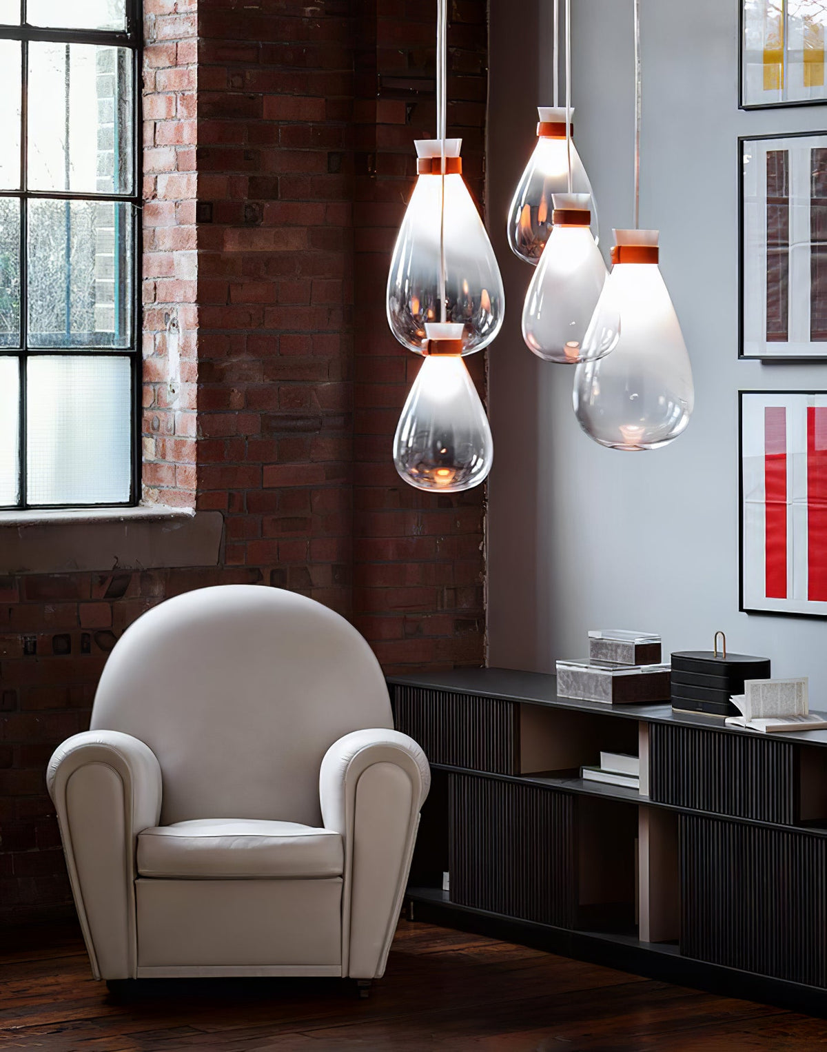 Clérachic teardrop pendants in a cluster beside a brick wall and a window, above a pale armchair and a dark shelf.
