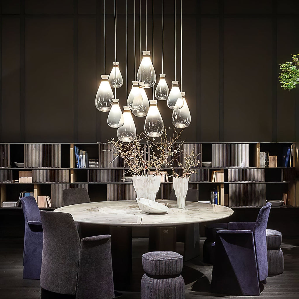 Large cluster of Clérachic teardrop pendants glowing above a round marble table with purple armchairs and tall shelves.