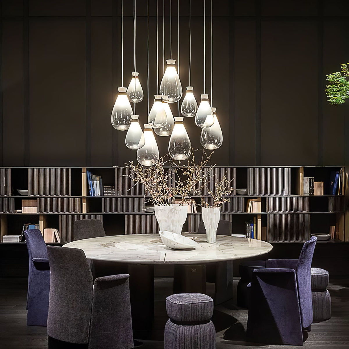 Large cluster of Clérachic teardrop pendants glowing above a round marble table with purple armchairs and tall shelves.