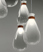 Close view of frosted-white Clérachic teardrop pendants with tan leather straps, lit at the neck against a grey backdrop.