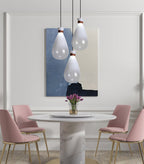 Three white Clérachic teardrop pendants above a round marble pedestal table with pink chairs and a blue abstract painting behind.