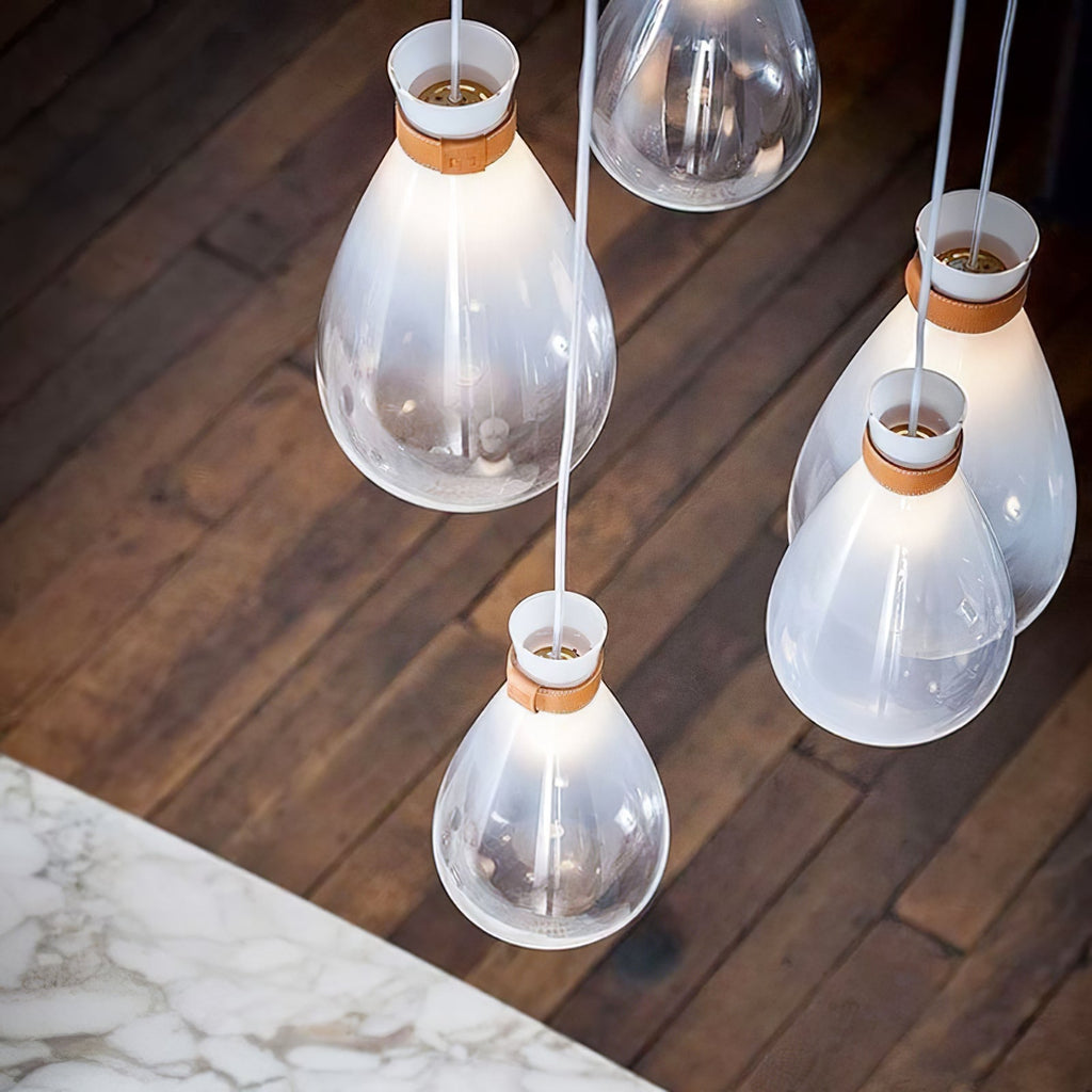 Looking down on four white Clérachic teardrop pendants with leather straps, above a dark wood floor and a marble table edge.