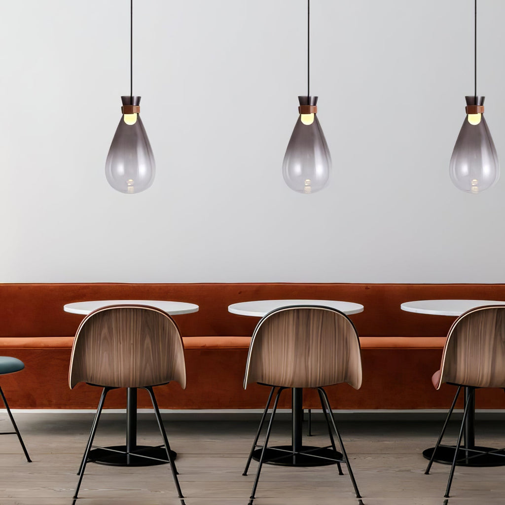 Three smoke-grey Clérachic teardrop pendants in a row above round tables, with walnut chairs and a rust-coloured bench seat.