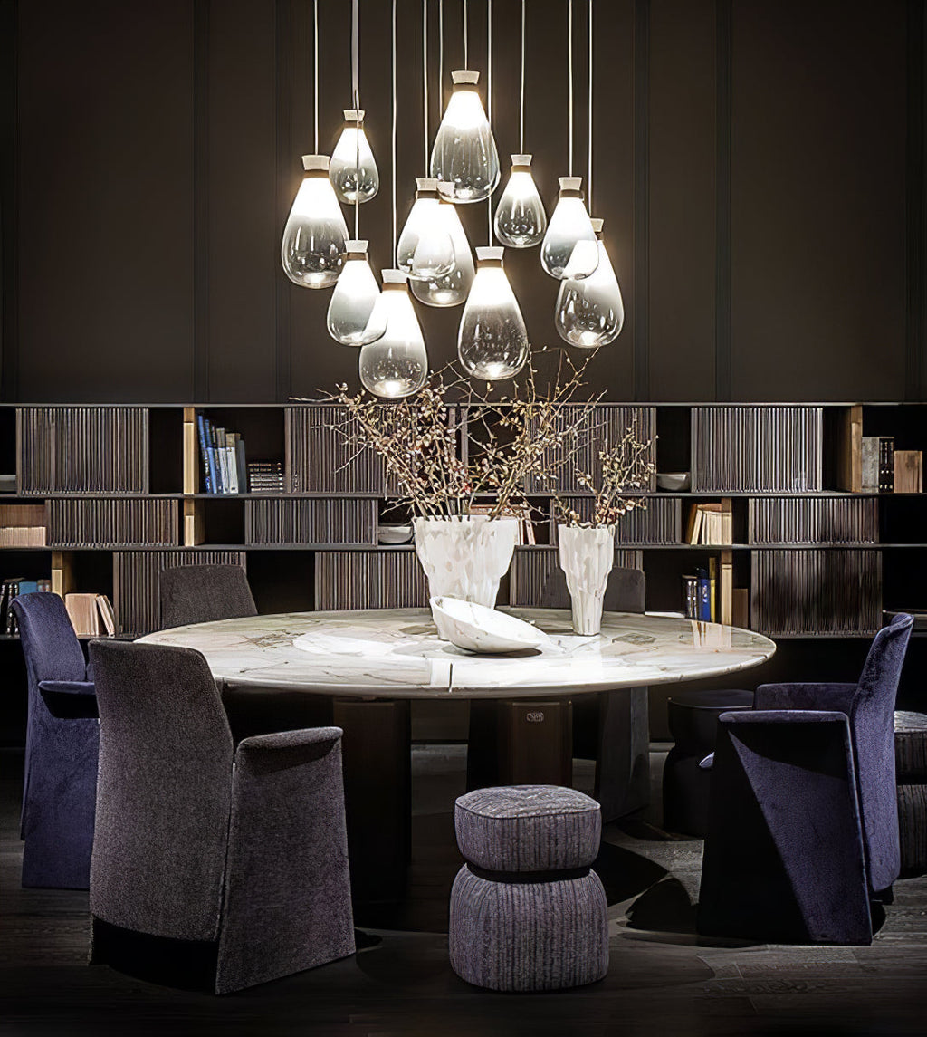 Cluster of clear and grey Clérachic teardrop pendants over a round table with purple armchairs, in front of shelves.