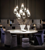 Cluster of clear and grey Clérachic teardrop pendants over a round table with purple armchairs, in front of shelves.