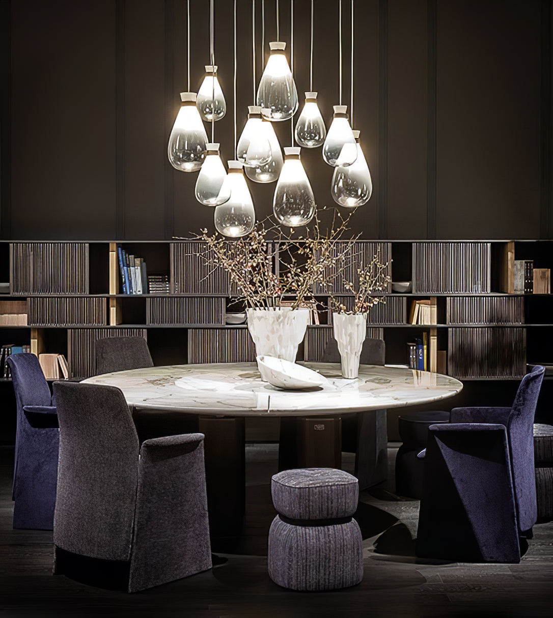 Cluster of clear and grey Clérachic teardrop pendants over a round table with purple armchairs, in front of shelves.