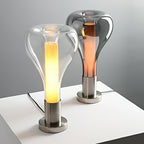 A clear teardrop lamp with a bright column stands in front of a smoke-grey one with an amber core, on a white surface, from Clérachic.