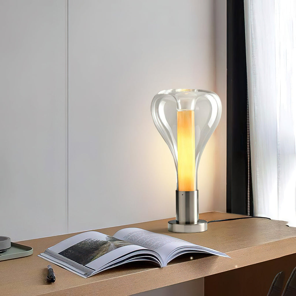 At a distance, this Clérachic clear glass teardrop lamp glows warm on a wooden shelf, with an open book and a pen in the foreground.