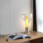 At a distance, this Clérachic clear glass teardrop lamp glows warm on a wooden shelf, with an open book and a pen in the foreground.