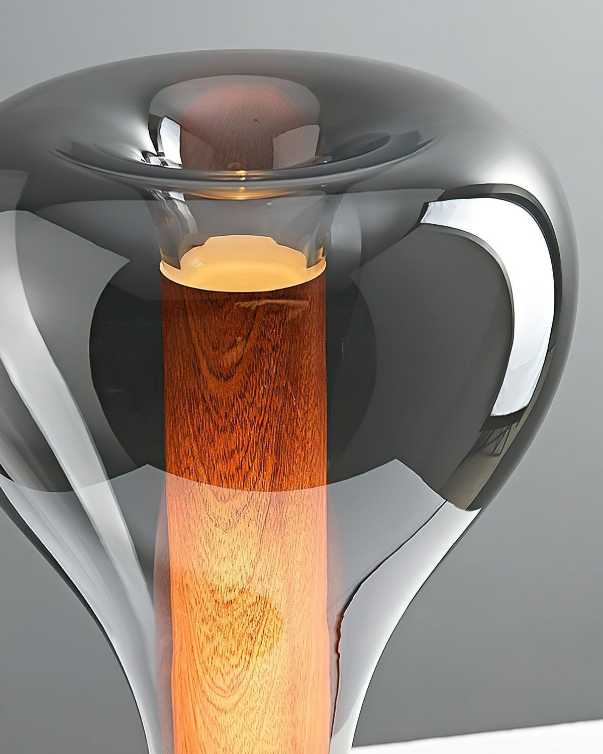 Close view of the smoke-grey glass shade and wood-grain amber core of this Clérachic lamp, with a soft glow at the top.
