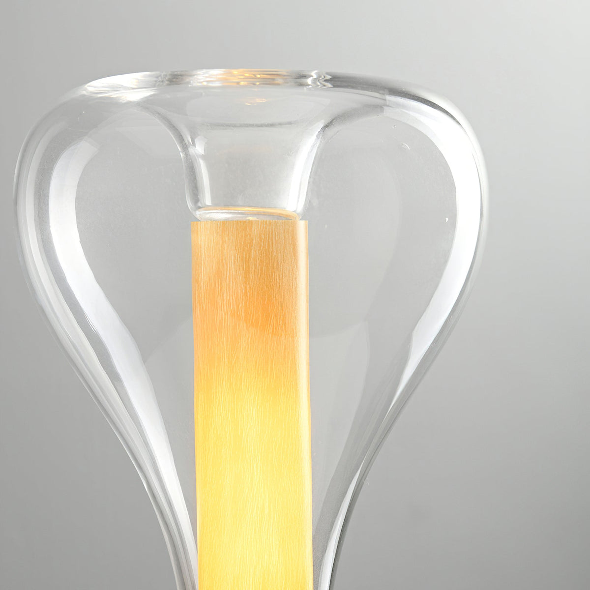 Close view of the clear glass shoulder and lit amber column inside this Clérachic lamp, against a pale grey backdrop.
