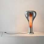A smoke-grey teardrop lamp with a glowing wood-toned core stands on a white sideboard with its black cord trailing, from Clérachic.