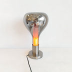A mirror-finish shade lit from within, with an amber glow through the glass, on a round chrome base with a black cord, from Clérachic.