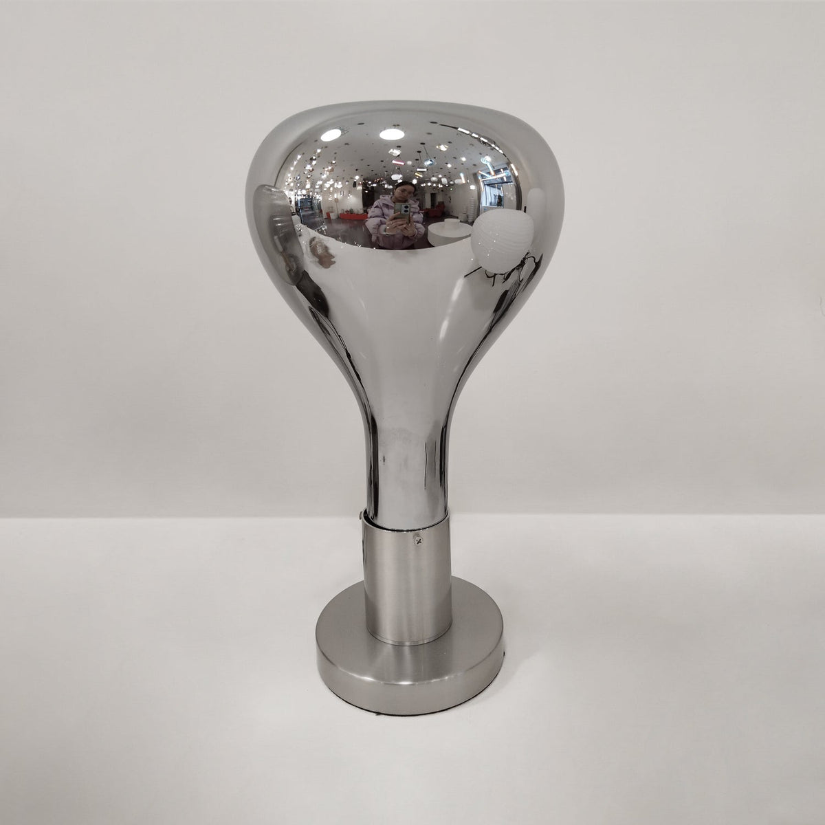 Tight view of a mirror-chrome teardrop shade and brushed stem, on a pale grey backdrop, from Clérachic.