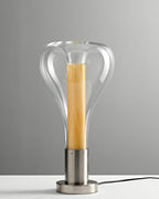Seen from slightly above, a clear teardrop glass lamp with a pale wood column sits on a chrome base and a grey cord, from Clérachic.