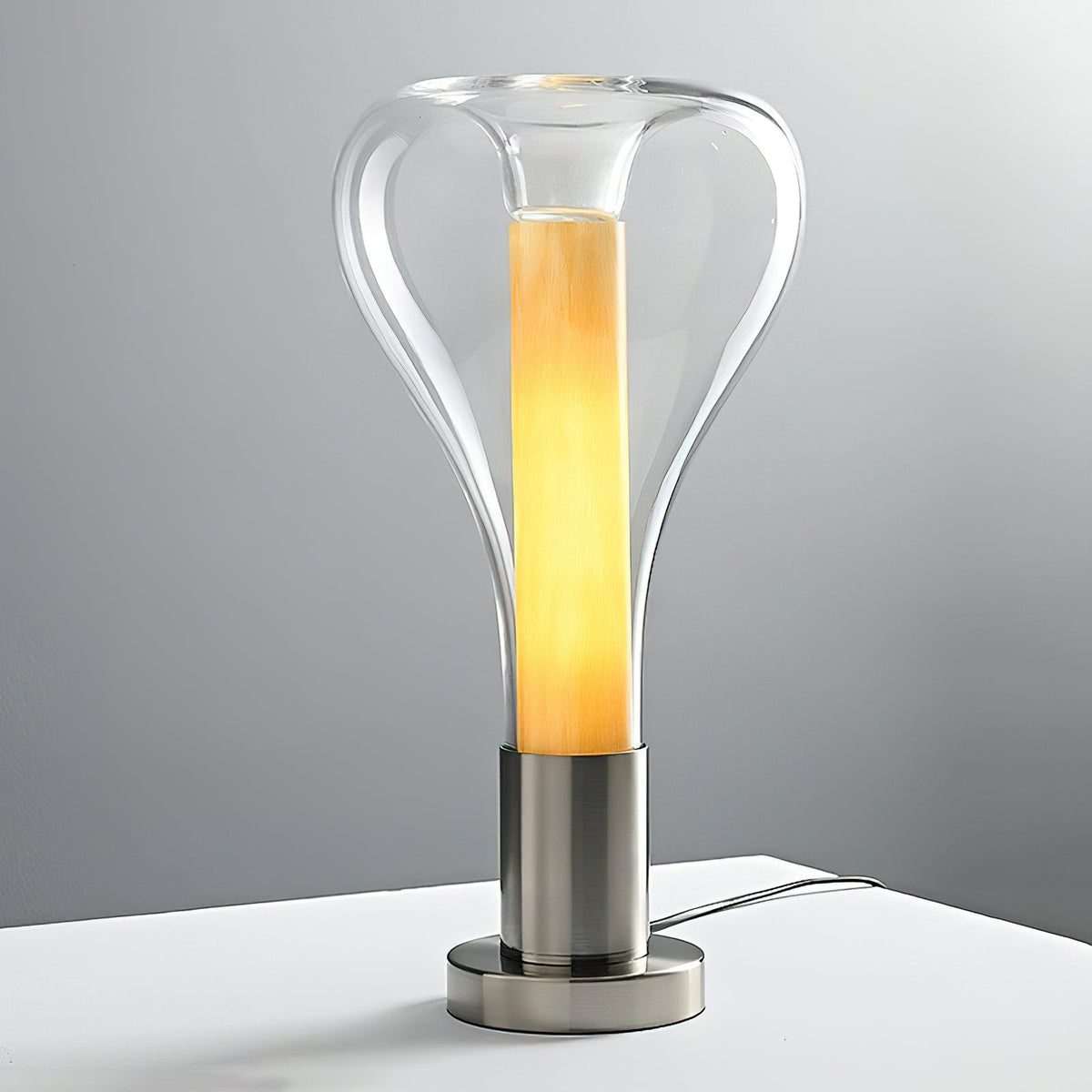 A clear glass teardrop lamp glows amber inside with a ribbed, wooden-looking core, on a chrome base with a cord, from Clérachic.