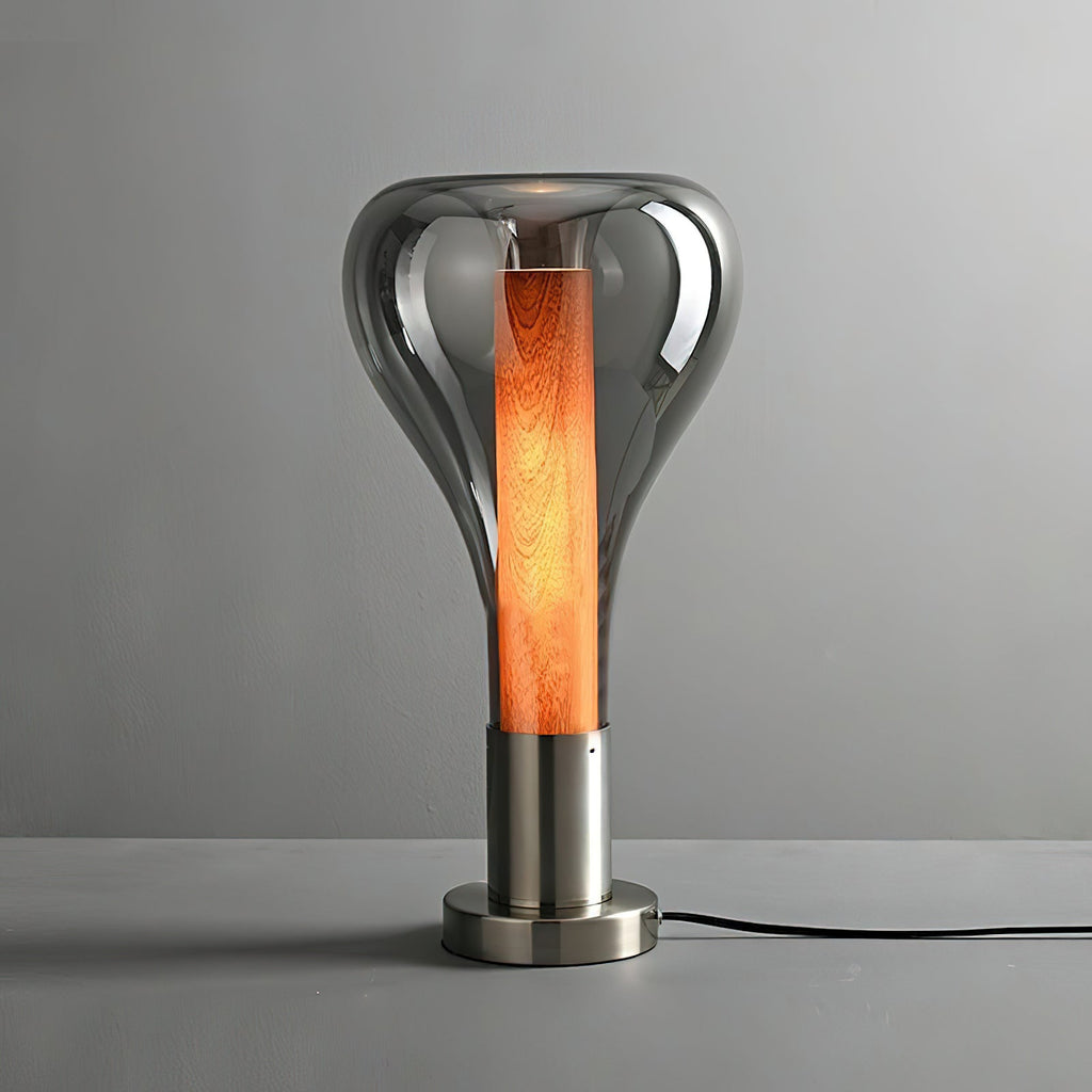 A smoke-grey teardrop lamp with a deep orange wooden core stands on a brushed metal base on a grey surface, from Clérachic.
