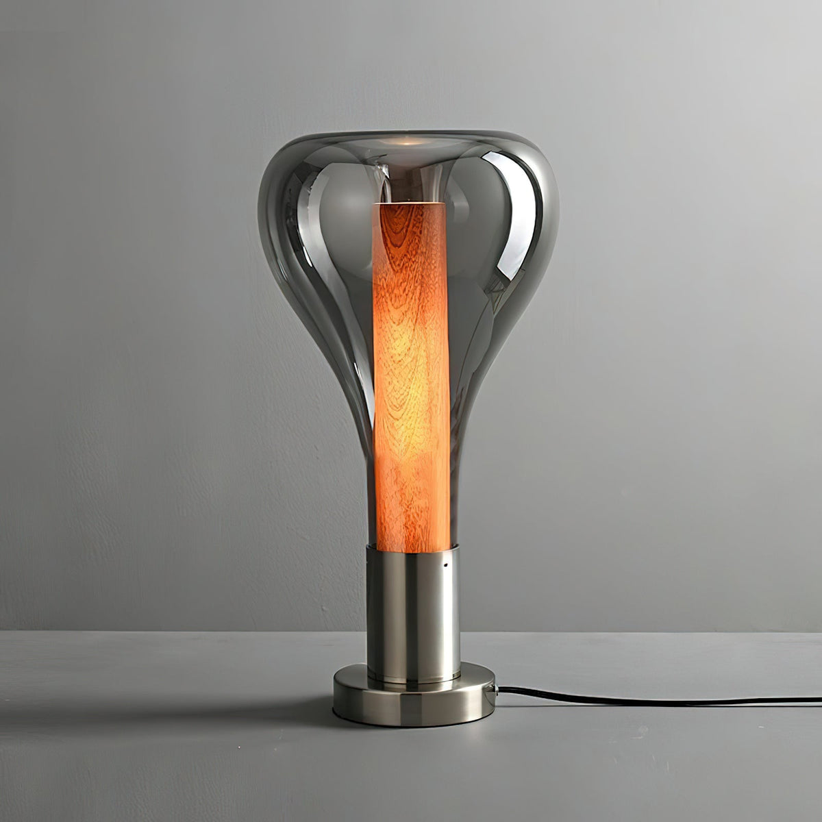 A smoke-grey teardrop lamp with a deep orange wooden core stands on a brushed metal base on a grey surface, from Clérachic.
