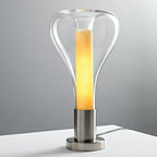 Seen straight on, a clear glass teardrop lamp glows with a bright amber column on a chrome base, from Clérachic.