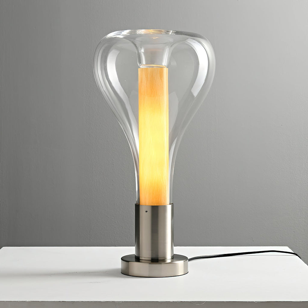 A clear teardrop lamp with a lit amber column on a chrome base, standing on a white shelf against grey, from Clérachic.