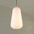 Clérachic teardrop glass pendant light in white opal, lit to a soft cream glow against a pale sage wall.