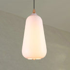 Clérachic teardrop glass pendant light in white opal, lit to a soft cream glow against a pale sage wall.