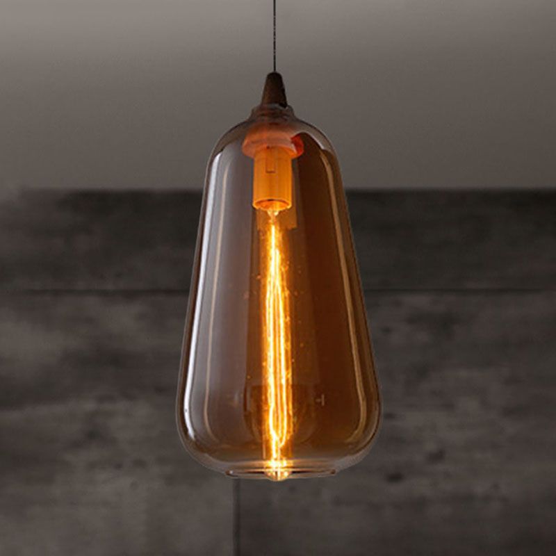 The Clérachic teardrop pendant in amber glass, filament glowing warm against a raw concrete wall.