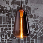 Clérachic teardrop pendant in smoke gray glass, lit warm, hanging against graphic city-map wallpaper.